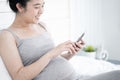 Beautiful pregnant woman using mobile phone in her bedroom. Royalty Free Stock Photo