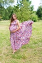 Beautiful pregnant woman walking barefoot in the park in long colorful dress with flying fabric. Happy maternity and fashion Royalty Free Stock Photo