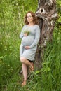Beautiful pregnant woman well dressed standing near the tree in the green park in sunny day