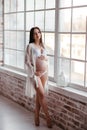 Beautiful pregnant woman in white bodysuit by the window. the beauty of the female body. cosmetics and sports, dancing for