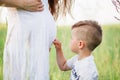 Beautiful pregnant woman in white dress on the meadow with her son Royalty Free Stock Photo