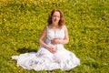 Beautiful pregnant woman in white dress relaxing in the green park in sunny day