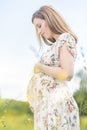 Beautiful pregnant woman in white summer dress in meadow full of yellow blooming flovers. Royalty Free Stock Photo