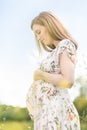 Beautiful pregnant woman in white summer dress in meadow full of yellow blooming flowers. Royalty Free Stock Photo