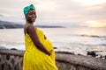 Beautiful pregnant woman in yellow fashionable dress posing on the beach, smiling and looking at the camera. Future motherhood Royalty Free Stock Photo