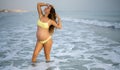 Beautiful pregnant woman in yellow swimsuit posing on the beach. Royalty Free Stock Photo