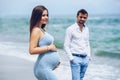 Beautiful pregnant woman in a blue tight dress touching her belly with love and care in the foreground and her