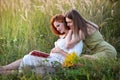 A beautiful pregnant woman and her friend are reading a book in the meadow. Concept of pregnancy, rest, relaxation