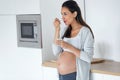 Beautiful pregnant young woman eating yogurt while standing in the kitchen at home Royalty Free Stock Photo