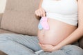 Beautiful pregnant young woman holding a pair of cute baby socks on her tummy, lying on sofa at home Royalty Free Stock Photo