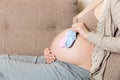 Beautiful pregnant young woman holding a pair of cute baby socks on her tummy, lying on sofa at home Royalty Free Stock Photo