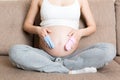 Beautiful pregnant young woman holding a pair of cute baby socks on her tummy, lying on sofa at home Royalty Free Stock Photo