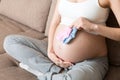 Beautiful pregnant young woman holding a pair of cute baby socks on her tummy, lying on sofa at home Royalty Free Stock Photo