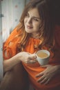 Beautiful pregnant young woman sitting in kitchen near window with cup of hot tea drink, motherhood concept Royalty Free Stock Photo