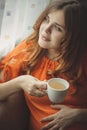 Beautiful pregnant young woman sitting in kitchen near window with cup of hot tea drink, motherhood concept Royalty Free Stock Photo