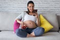 Beautiful pregnant young woman using her mobile phone while eating strawberries on sofa at home Royalty Free Stock Photo