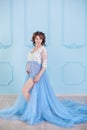 Beautiful pregnant young woman wearing luxury blue lingerie dress, studio portrait of amazing lady with curly brunette hairs Royalty Free Stock Photo