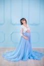Beautiful pregnant young woman wearing luxury blue lingerie dress, studio portrait of amazing lady with curly brunette hairs Royalty Free Stock Photo