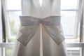 Beautiful pretty big bow on front of brides bright elegant white wedding dress hanging up in the window Royalty Free Stock Photo