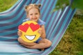A beautiful pretty girl smiles sitting on hammock and holds a paper smile face Royalty Free Stock Photo