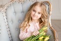 Beautiful pretty girl with yellow flowers tulips sitting in arm-chair, smiling. Indoor photo Royalty Free Stock Photo