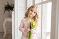 Beautiful pretty girl with yellow flowers tulips standing near big window, smiling. Indoor photo. Spring theme. Close-up. Nice Royalty Free Stock Photo