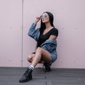 Beautiful pretty young brunette in sunglasses in a trendy vintage blue skirt in a stylish black top in a denim jacket Royalty Free Stock Photo