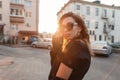 Beautiful pretty young hipster woman in trendy clothes in retro style in fashionable dark sunglasses is posing outdoors