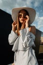 Beautiful pretty young woman in fashion striped dress in stylish sunglasses in vintage straw hat posing outdoors on bright sunny Royalty Free Stock Photo