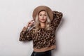 Beautiful pretty young woman in a trendy stylish leopard sweater in trendy black leather pants and a beige hat posing indoors Royalty Free Stock Photo