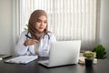 A beautiful Asian Muslim female doctor is working on her laptop at her desk at a hospital or clinic Royalty Free Stock Photo