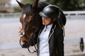 Beautiful professional female jockey standing near horse. woman horse rider is preparing to equitation