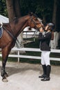 Beautiful professional female jockey standing near horse. woman horse rider is preparing to equitation