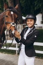 Beautiful professional female jockey standing near horse. woman horse rider is preparing to equitation