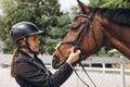 Beautiful professional female jockey standing near horse. Woman horse rider is preparing to equitation