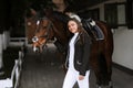 Beautiful professional female jockey standing near horse. woman horse rider is preparing to equitation. Girl and horse