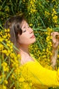 Beautiful profile portrait of a woman in a yellow suit among the bright mimosa flowers, enjoying the sunlight with her eyes closed