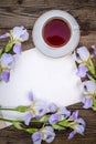 Beautiful purple flowers irises, a sheet of paper and a cup of tea on a wooden background
