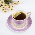 Beautiful purple tea cup with lemon and white flowers in background Royalty Free Stock Photo