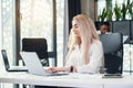 Pretty purposeful young female office manager entering datas from financial report to laptop in the modern office