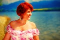Beautiful radiant girl with red hair and colorful sommer dress beside a lake.