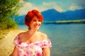 Beautiful radiant girl with red hair and colorful sommer dress beside a lake.