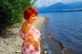 Beautiful radiant girl with red hair and colorful sommer dress beside a lake.