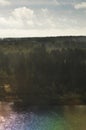 Beautiful rainbow-colored water and green forests pictured from airplane window with blue sky and clouds. Countryside view or a