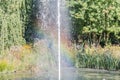 Beautiful rainbow reflected in the water of a fountain and surrounded by trees