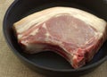 Appetizing raw pork steak in a round black pan is ready for frying. Angle view