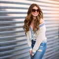 Beautiful real model woman with friendly smile wearing casual clothes, jeans and sunglasses posing outdoors near a wall.