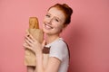 Beautiful red-haired girl with gathered hair in an apron smiles broadly holding a packet of bread in her hands Royalty Free Stock Photo