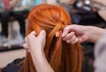 Beautiful red-haired girl, hairdresser weave a French braid close-up Royalty Free Stock Photo