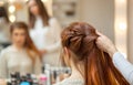 Beautiful, red-haired girl with long hair, hairdresser weaves a French braid, in a beauty salon Royalty Free Stock Photo